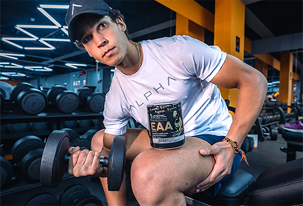 Hombre sosteniendo mancuerna y suplemento EAA en gimnasio