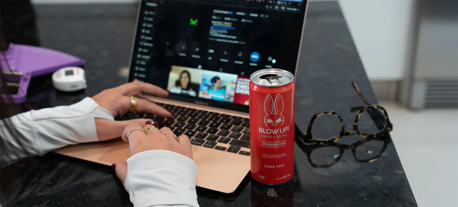 Laptop dorada, bebida energética roja y gafas en una superficie negra