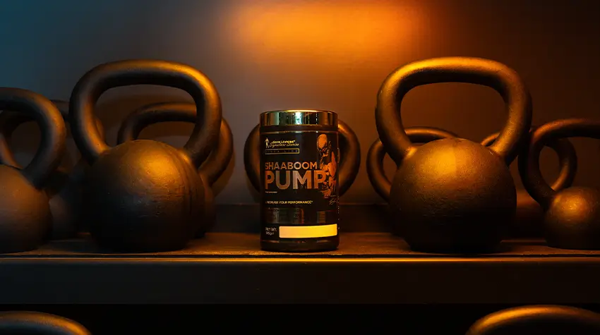 Suplemento BHAABOOM PUMP en polvo junto a kettlebells en un gimnasio